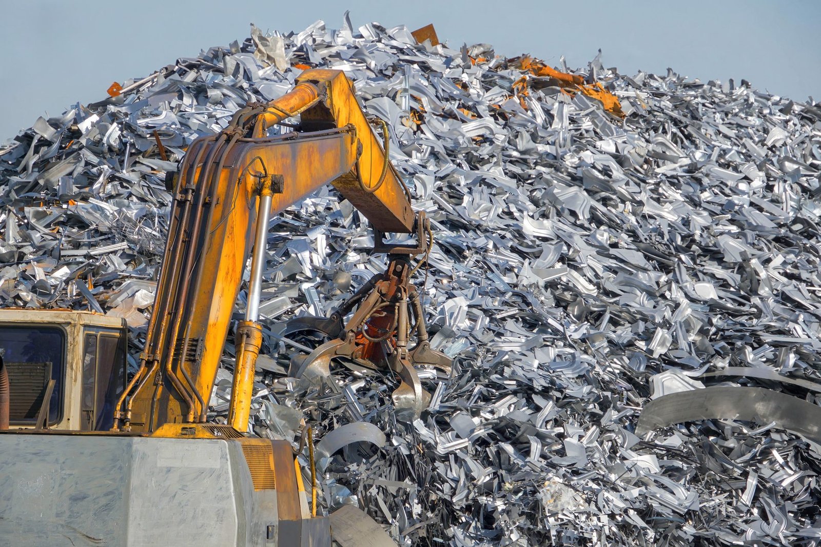 Scrap metal recycling yard with excavator handling a large pile of aluminium scrap
